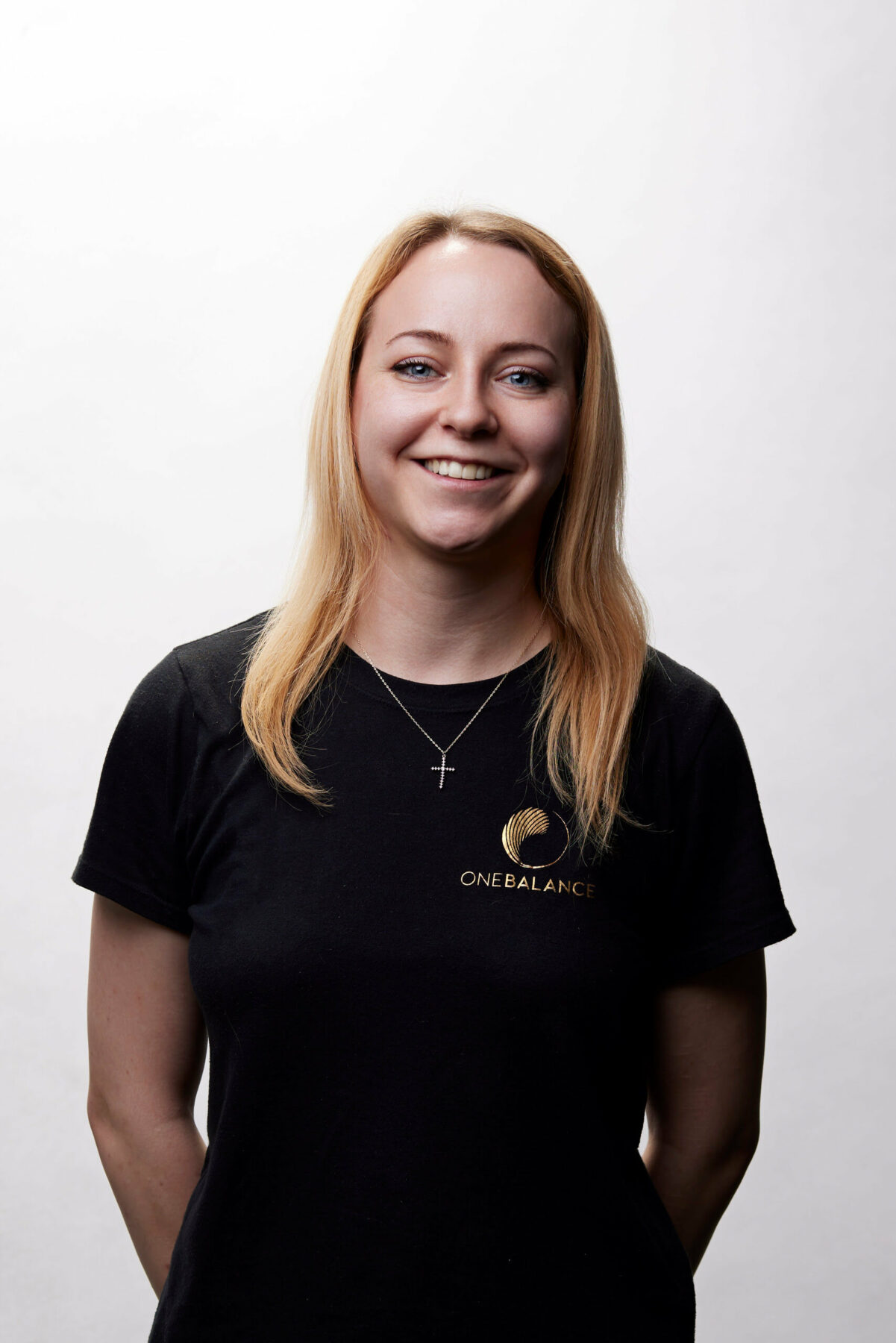 Studio-Porträt einer lächelnden Frau mit blondem Haar im schwarzen T-Shirt vor hellem Hintergrund.