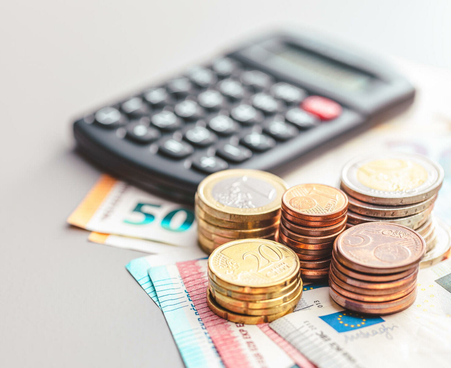 Gestapelte Euro-Münzen und Geldscheine mit Taschenrechner als Symbol für Budgetplanung, Finanzen und Sparen.