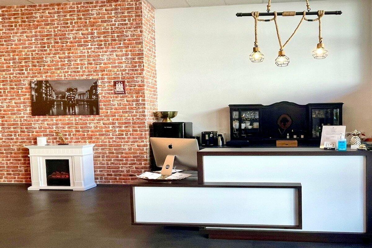 Empfangsbereich mit weißer Theke, Backsteinwand, dekorativem Kamin und drei Hängelampen im Industrial-Stil.