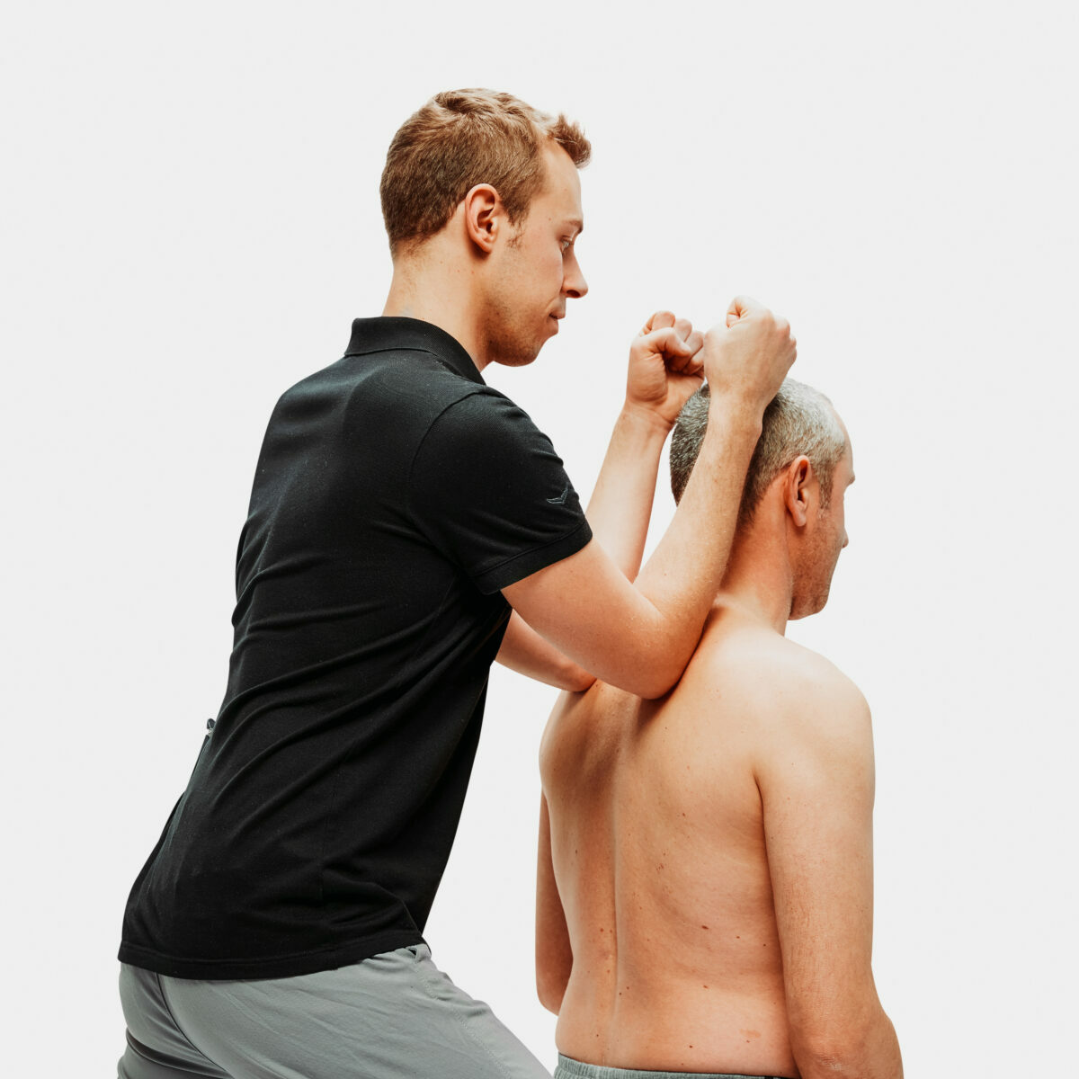 Physiotherapeut führt manuelle Therapie am Nacken eines sitzenden Mannes durch, Fokus auf Schulter- und Halsbereich.
