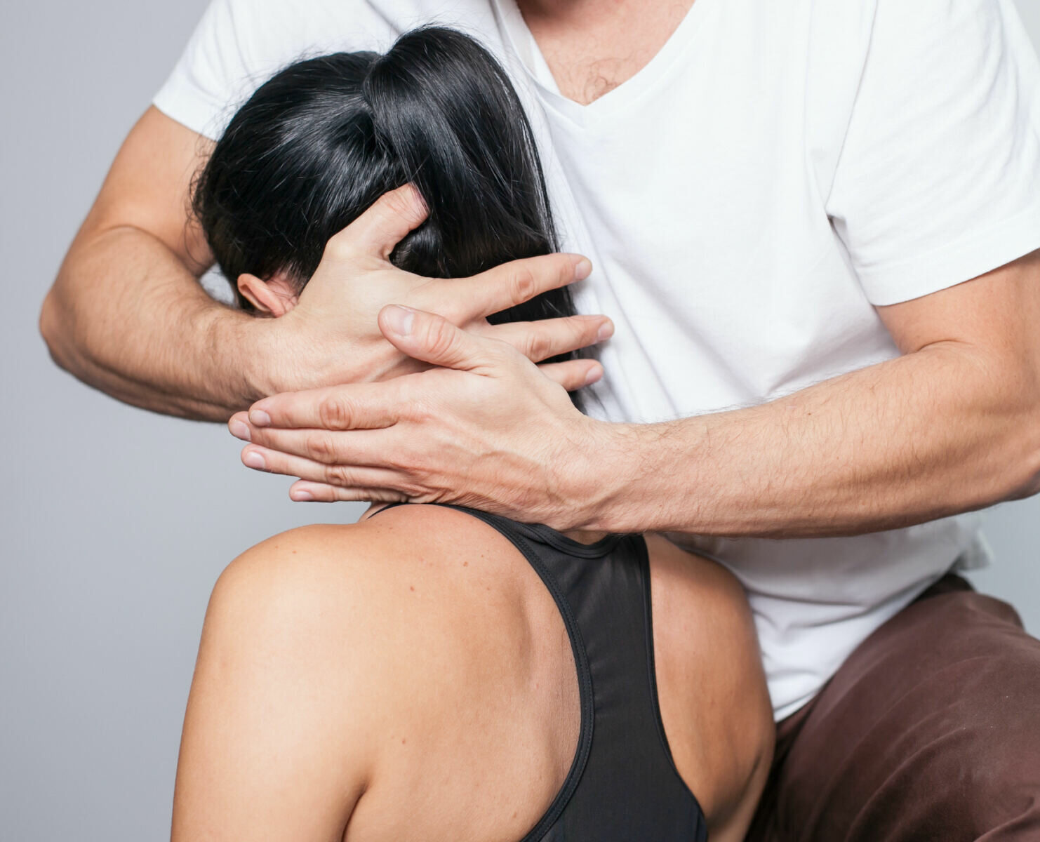 Therapeut führt manuelle Nackenbehandlung bei Patientin durch, Hände stabilisieren Kopf und Hals zur Mobilisation.