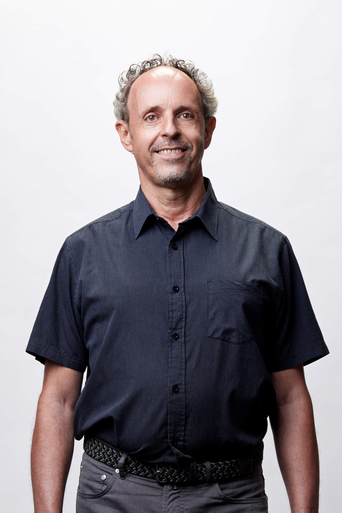 Studio-Porträt eines lächelnden Mannes mit kurzärmligem Hemd vor hellem, neutralem Hintergrund.