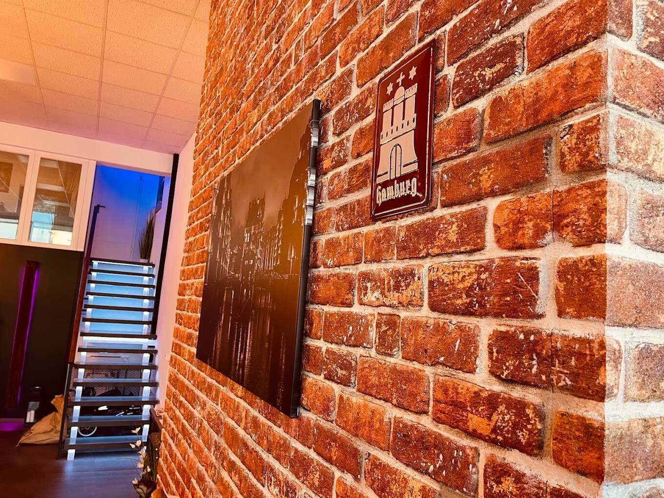 Backsteinwand im Eingangsbereich mit Hamburg-Schild und Treppe, stimmungsvolle Beleuchtung in der Physiotherapiepraxis onebalance hamburg